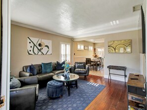 Ein Wohnzimmer mit Ledersofa, Hocker und Couchtisch, ein Essbereich mit Stühlen und Tisch sowie Kunstwerke an den Wänden.