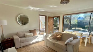 A living room with two sofas, a round mirror, a dining table with chairs, and large windows. - The Deck @ VB - Linen, Wi-Fi, Pets, Secured Yard (Venus Bay)