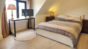 Une chambre à coucher avec un lit, un bureau avec un ordinateur, une lampe et une fenêtre avec des rideaux.