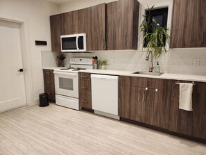 A modern kitchen with wooden cabinets, a white microwave, a stove, and a dishwasher.