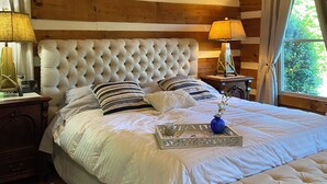 Une chambre avec un grand lit, des murs recouverts de panneaux de bois, un ventilateur de plafond et une fenêtre avec des rideaux.