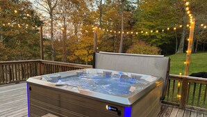 Un bain à remous sur une terrasse en bois, agrémentée d’une rambarde en bois et de guirlandes lumineuses.