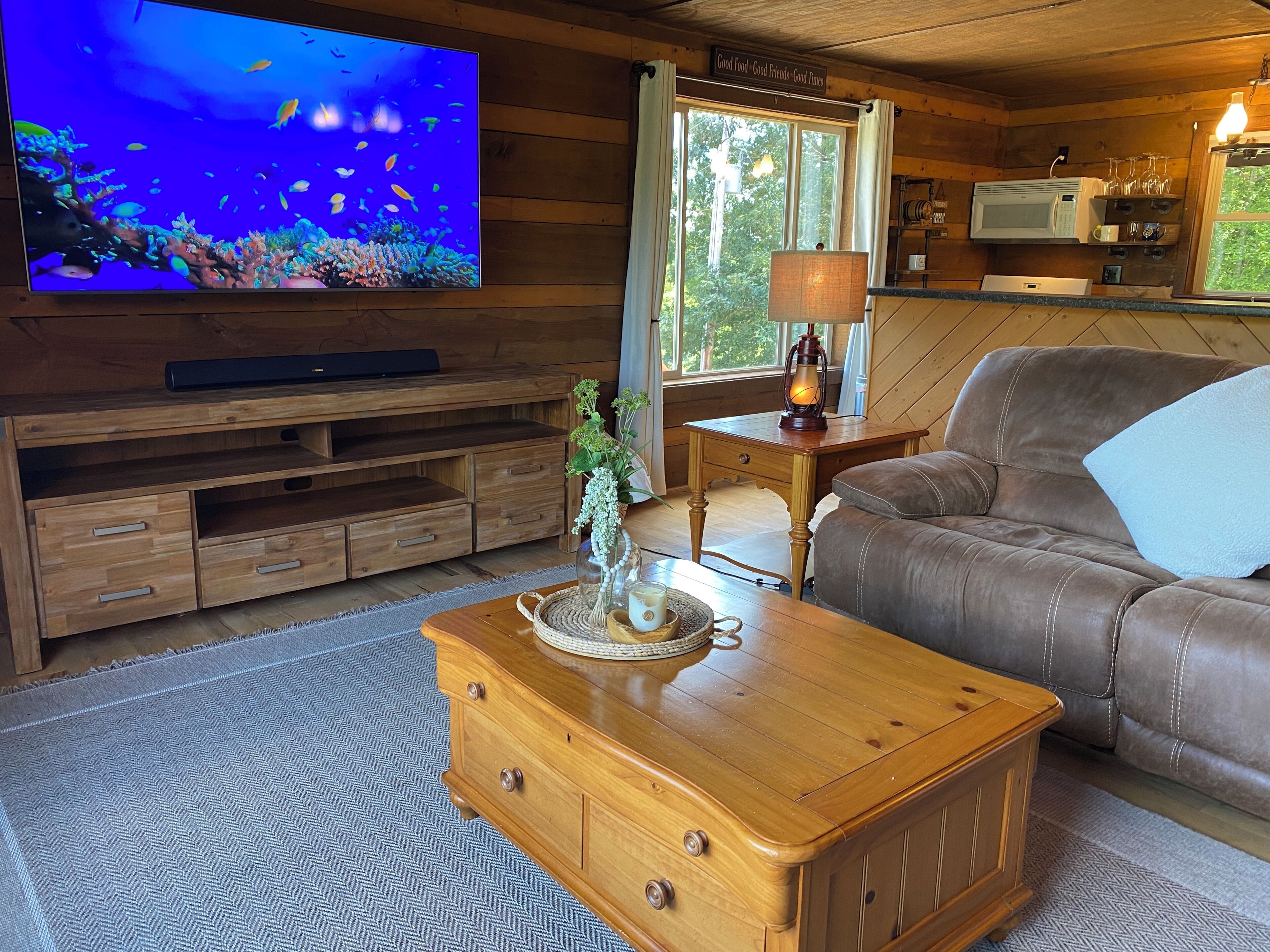 A cozy living room with a wooden TV stand, a leather sofa, a wooden coffee table, and a window with curtains.
