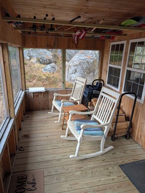 A wooden cabin with rocking chairs, a small table, and a view of the outdoors. - Maine, off the grid Cabin Sleeps up to 8 people. Moxie Pond West Forks (West Forks)