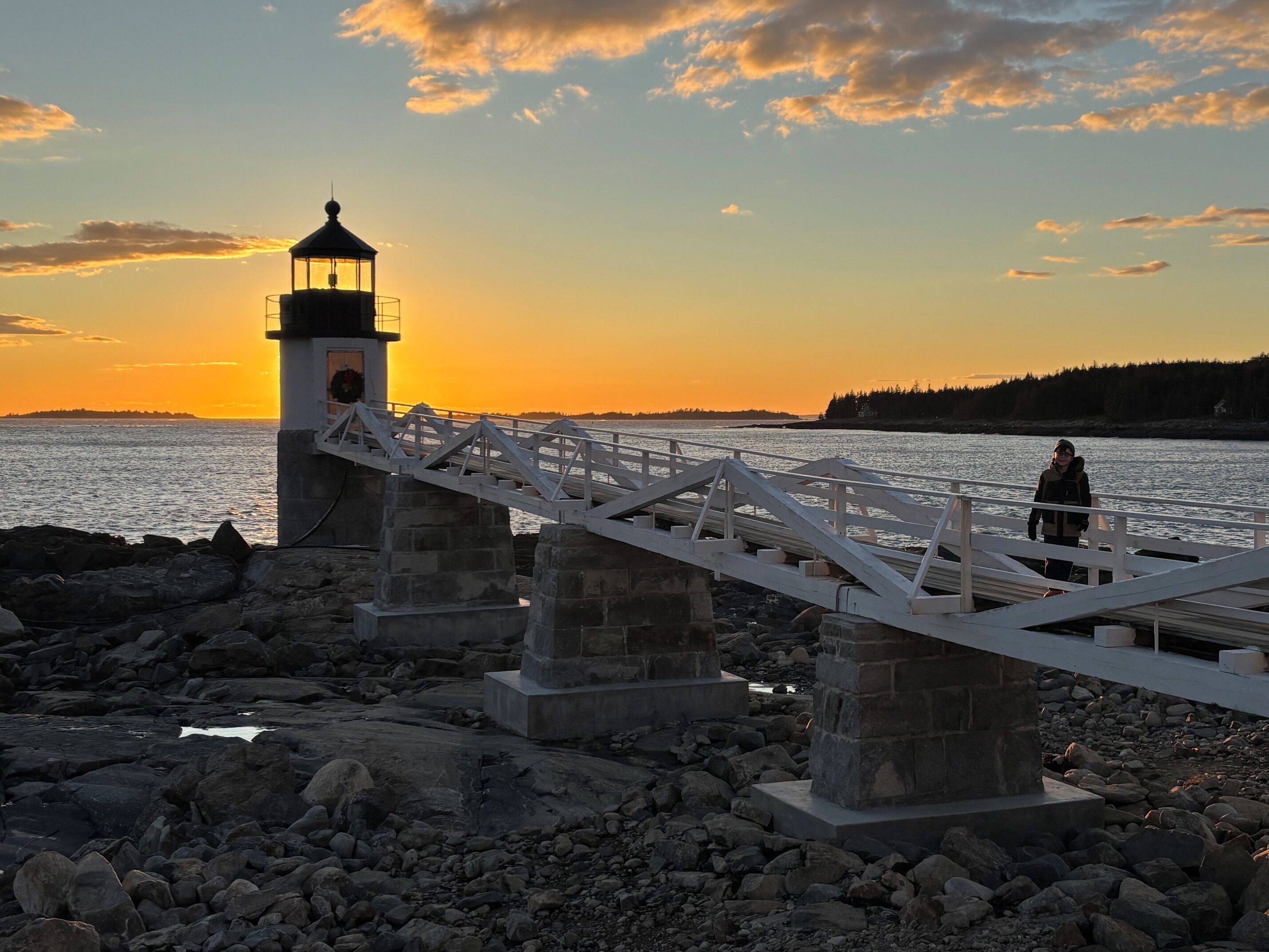 A lighthouse on a rocky shore with a wooden bridge leading to it.