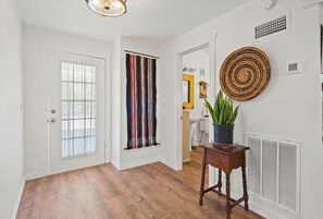A hallway with a wooden floor, a door with a window, a striped curtain, a round woven wall hanging, and a potted plant on a small table. - 2-bedroom house with acreage in tranquil Aripeka-Spring Hill area with AC (Spring Hill)