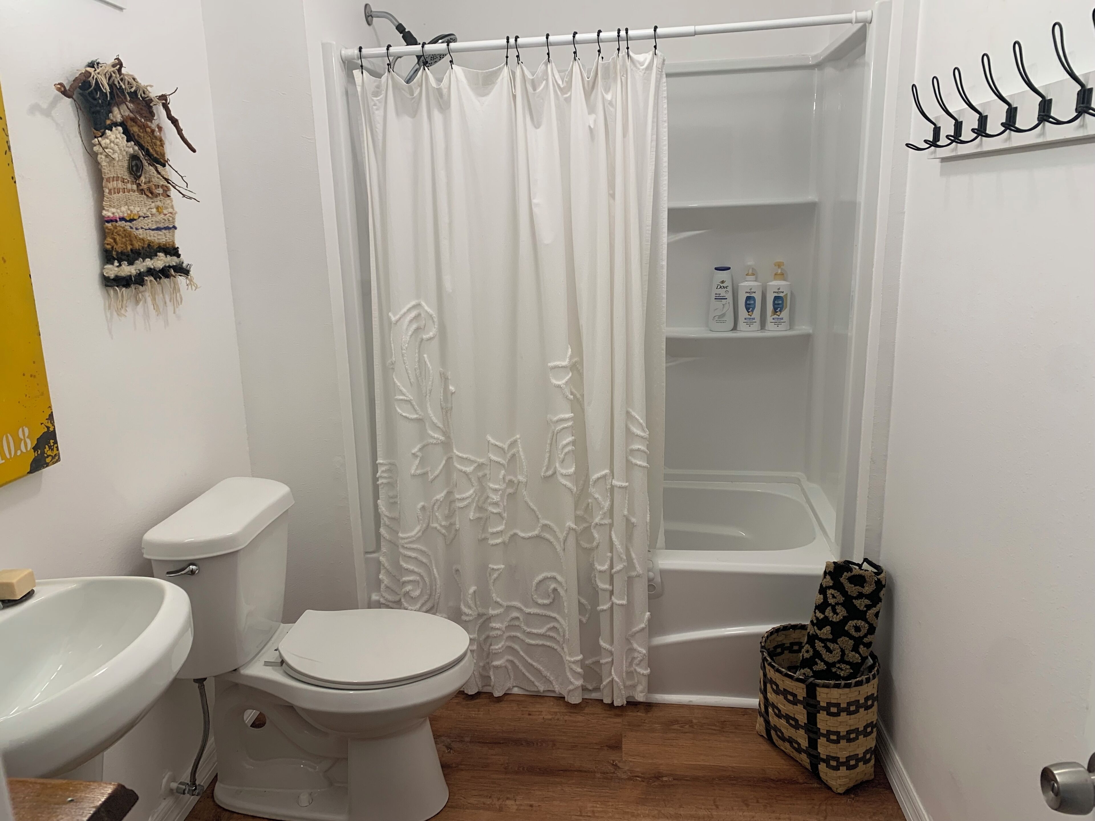 Un baño con inodoro, lavamanos, cortina de ducha y estante con artículos de tocador.