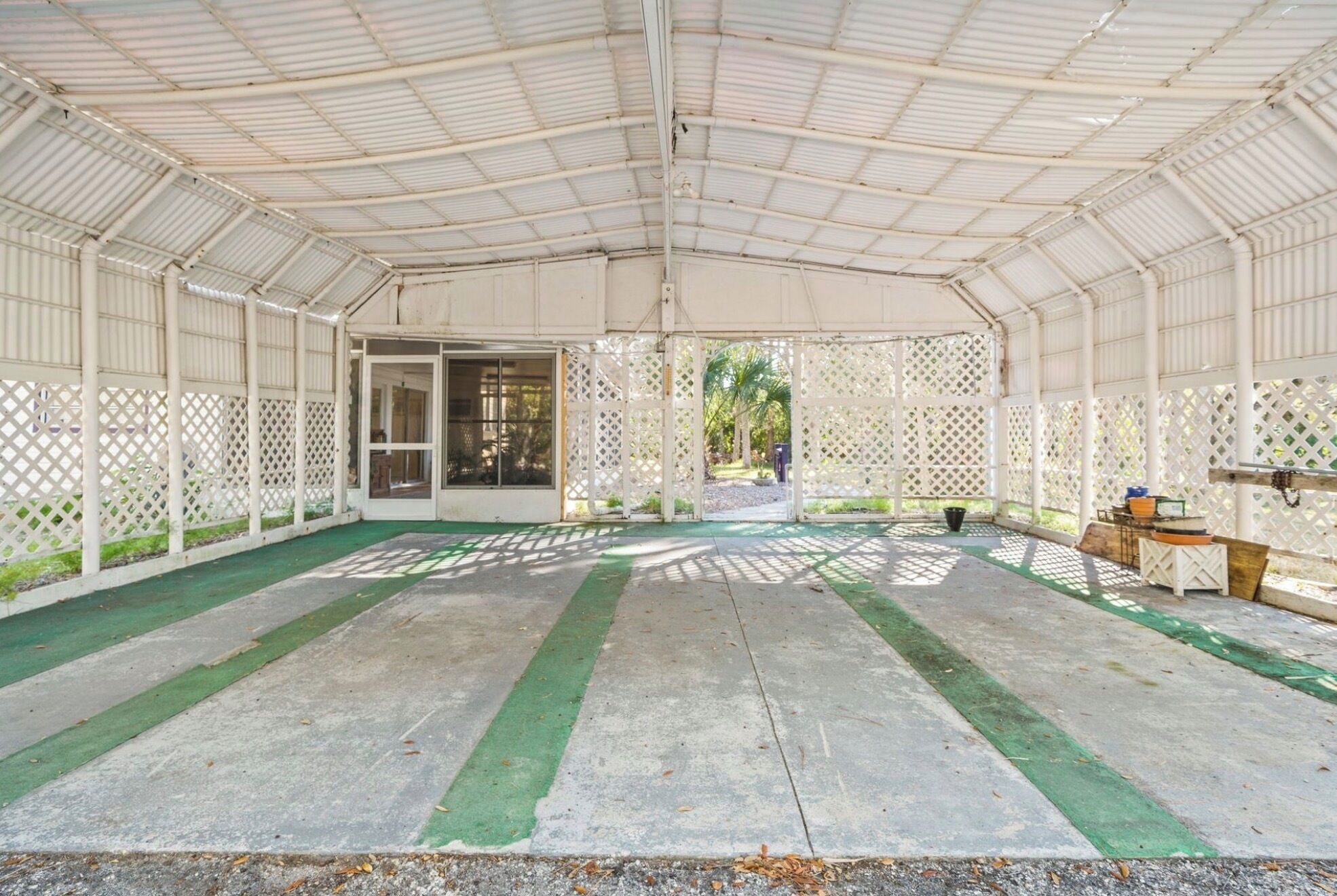 A covered outdoor area with a concrete floor, lattice panels, and a door leading outside.