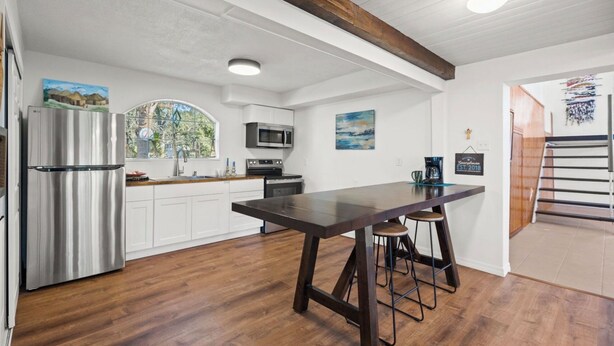 A kitchen with white cabinets, a stainless steel refrigerator, a wooden table, and a bar stool.