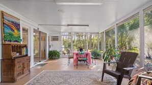A sunroom with a table and chairs, large windows, and a wooden cabinet with a colorful artwork.