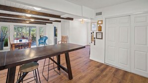A spacious kitchen with a long wooden table, a dining area with chairs, and a white door.