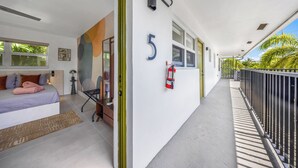Una habitación de hotel con cama, escritorio, silla, ventana, balcón y extintor.