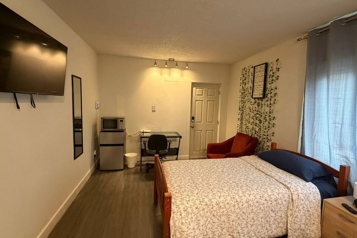 A compact hotel room with a bed, a desk, a chair, a television, and a door.