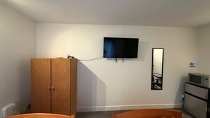 A room with a wooden wardrobe, a television mounted on the wall, a mirror, and a microwave. - Private Room Downtown with Kitchenette (Edmonton)