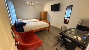 A hotel room with two single beds, a desk with a chair, a TV mounted on the wall, and a window with curtains. - Private Room Downtown with Kitchenette (Edmonton)
