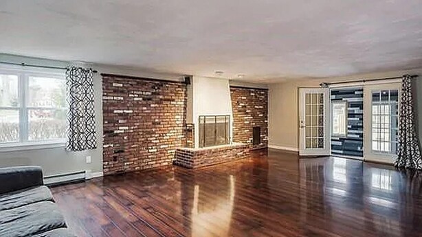 A spacious room with hardwood flooring, a brick accent wall, a fireplace, and a sliding glass door leading to an outdoor area. - World Cup Boston Private 6-Acre Estate Sleeps 16 Less than 18 Min From Gillette (Taunton)