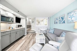 A modern kitchen with grey cabinets, a built-in microwave, and a flat-screen TV. - Experience Oceanfront Balcony Sunrises (North Myrtle Beach)
