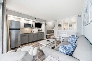 A modern kitchen with stainless steel appliances, a dining area with white furniture, and a living room with a gray sofa and patterned pillows. - Experience Oceanfront Balcony Sunrises (North Myrtle Beach)