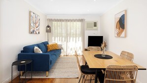 Ein modernes Wohnzimmer mit einem blauen Sofa, einem Esstisch mit Stühlen, einem Fernseher und Kunstwerken an den Wänden.
