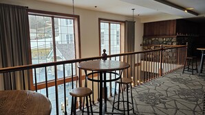A room with a wooden railing, a round table with stools, and large windows with curtains. - Year-round fun!  Condo at Jiminy Peak Resort.  Treat yourself! (Hancock)