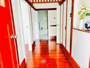 A hallway with wooden flooring, a red door, and a white wall with a globe and flowers. - Spacious 5 Bedrooms Fully Fenced house in Auckland (Mount Roskill)