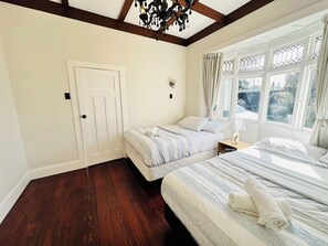 A bedroom with two beds, a wooden floor, a white door, and a window with curtains. - Spacious 5 Bedrooms Fully Fenced house in Auckland (Mount Roskill)