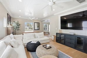 A modern living room with a sectional sofa, a flat-screen TV, ceiling fans, and a large window. - 5 Min to Atlantic Ave & Beach - Pool + Sauna Retreat (Delray Beach)
