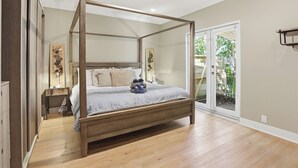 Una cama con dosel y estructura de madera, una mesita de noche con lámpara y vistas al exterior a través de un ventanal.