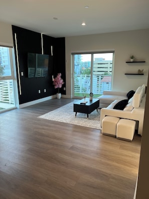 A modern living room with a sofa, a coffee table, a TV mounted on the wall, and a view of the outside through large windows. - BEAUTIFUL DOWNTOWN HOLLYWOOD BEACH YOUNG CIRCL 2B 2B Apt (Hollywood)