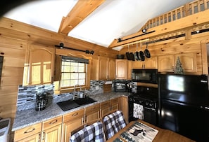 A kitchen with wooden cabinets, a granite countertop, a black refrigerator, and a dining area with plaid chairs.