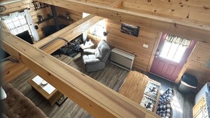 A loft-style room with wooden walls, a chandelier, a couch, a dining table, and a fireplace. - Cozy, peaceful cabin retreat with hot tub (Weld)