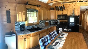 A kitchen with wooden cabinets, a granite countertop, a black refrigerator, and a dining area with a table and bench. - Cozy, peaceful cabin retreat with hot tub (Weld)