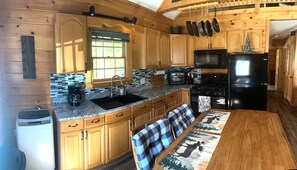 A kitchen with wooden cabinets, a granite countertop, a black refrigerator, and a dining area with a table and bench. - Cozy, peaceful retreat with hot tub (Weld)