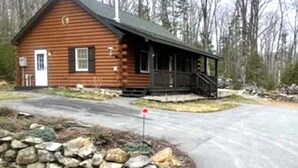 A wooden cabin with a porch, a stone wall in front, and a forested background. - Cozy, peaceful cabin retreat with hot tub (Weld)