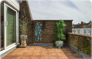 Eine Dachterrasse mit Backsteinmauer, Topfpflanzen und einem Fenster.