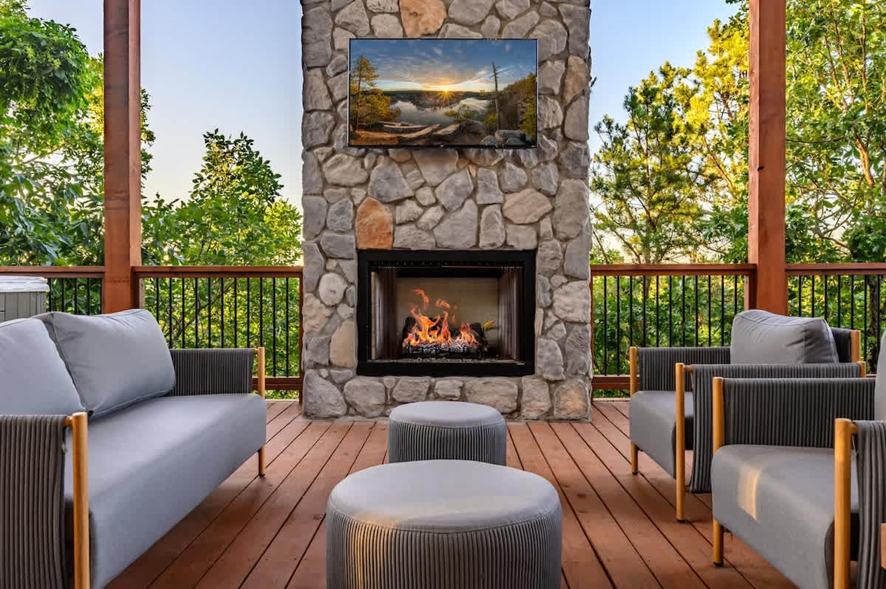 A stone fireplace with a fire, surrounded by outdoor furniture on a wooden deck.