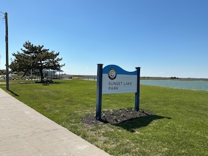 Un panneau d’information dans un parc, offrant une vue dégagée sur un lac, une zone herbeuse et un chemin pavé.