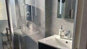 Un baño moderno con cabina de ducha de vidrio, un lavamanos blanco con espejo y muebles de almacenamiento oscuros.
