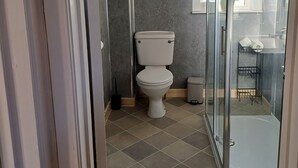 Un baño con inodoro, ducha y puerta de vidrio que da a un balcón.