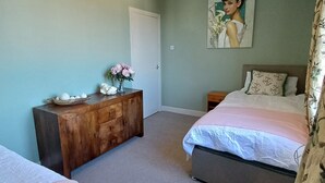 Un dormitorio con dos camas, un aparador de madera, un cuadro en la pared y una lámpara en el techo.
