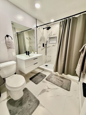 A modern bathroom with a toilet, sink, mirror, shower, and a towel rack. - Charming Relaxing Modern Retreat in Sunrise (Sunrise)