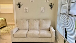 Un salon avec un canapé beige, un tapis vert et blanc, une plante en pot et des œuvres d’art murales.