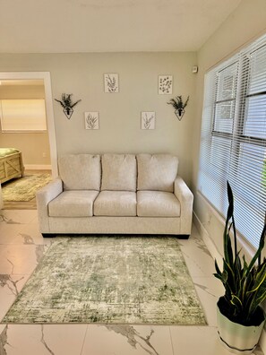 A living room with a beige sofa, a green and white rug, a potted plant, and wall art. - Charming Relaxing Modern Retreat in Sunrise (Sunrise)