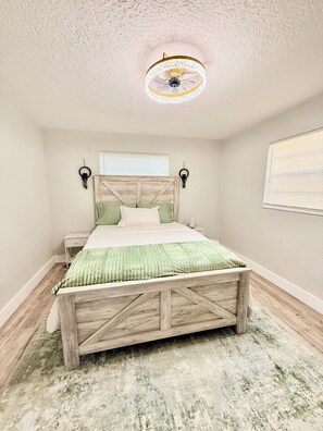 A bedroom with a wooden bed, a ceiling fan, a nightstand, and a wall-mounted lamp. - Charming Relaxing Modern Retreat in Sunrise (Sunrise)