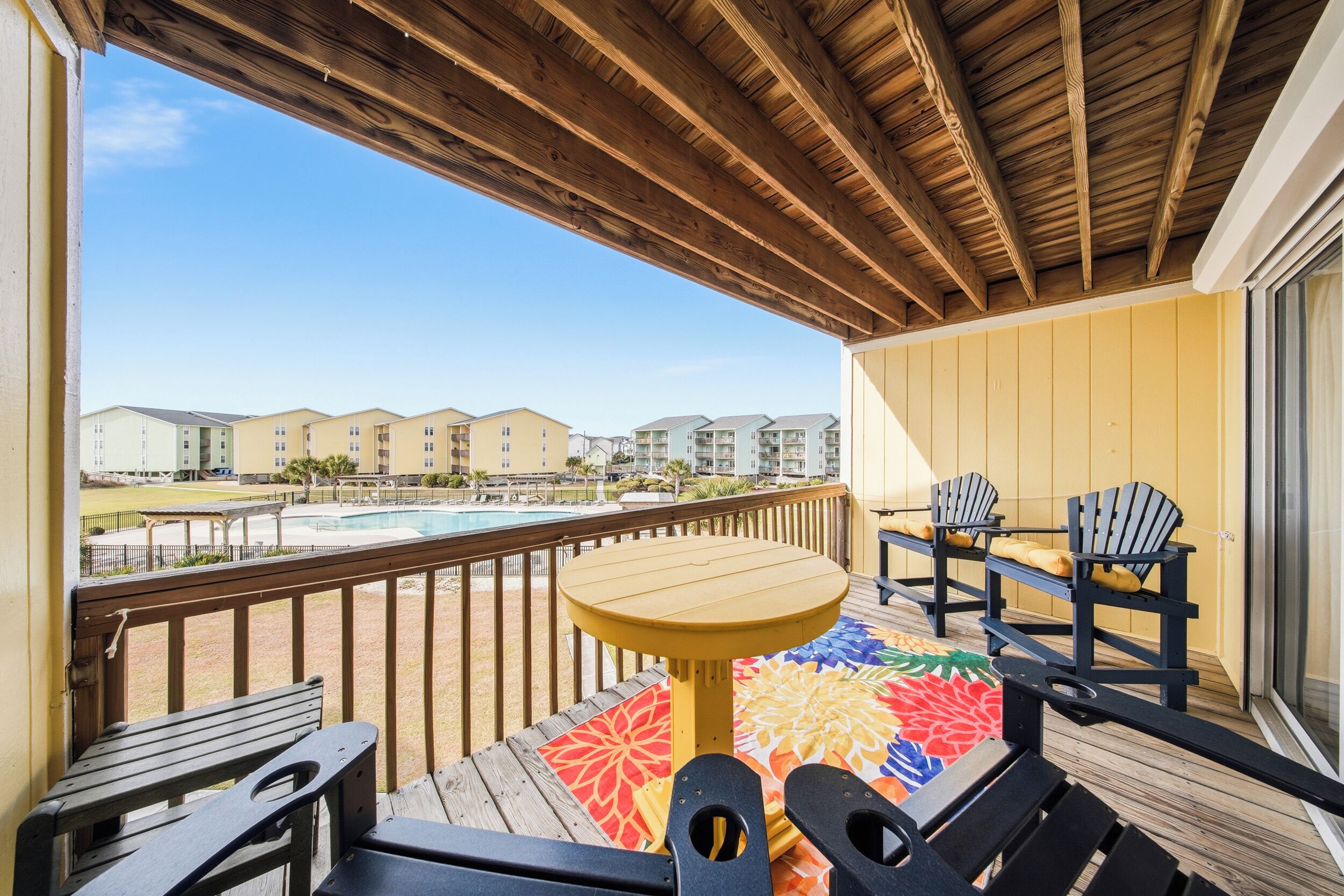 A wooden deck with a pool view, outdoor seating, and a view of multi-story buildings.