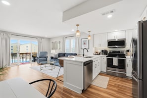 A modern kitchen with a central island, stainless steel appliances, and a dining area with a table and chairs. - Surf City Luxury Condo · Ocean Views · Pool (Surf City)