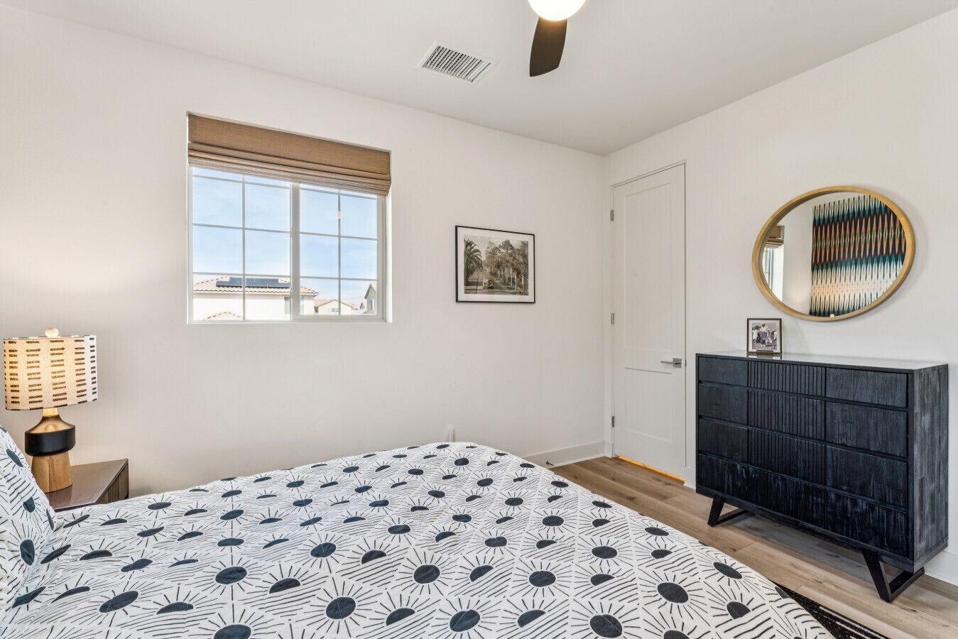 A bedroom with a bed, a dresser, a window with blinds, a framed picture on the wall, and a ceiling light.