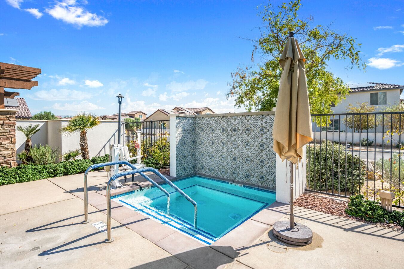 A swimming pool with a blue mosaic tile wall, a metal ladder, and a beige umbrella.