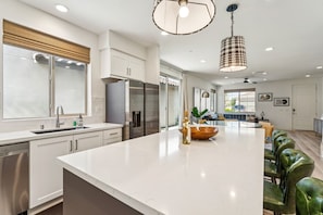 A modern kitchen with a central island, stainless steel appliances, and a dining area with green leather chairs. - Furnished Patio + Putting Green: La Quinta Home (La Quinta)