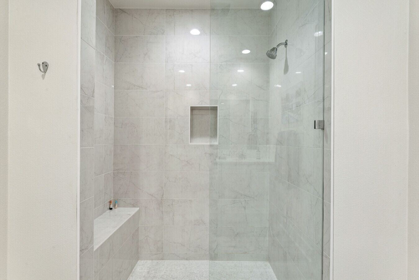 A modern shower with a glass door, a built-in shelf, and a recessed ceiling light.